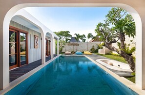 A modern pool area with a clear view of the pool, a wooden deck, and a stone wall. - Navya Villas (Kerobokan)
