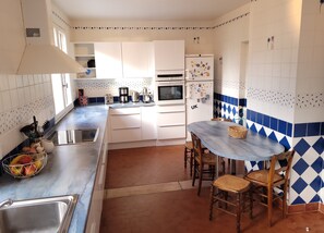 Modern kitchen with stainless steel sink, oven, microwave, and refrigerator, complemented by a blue and white tiled backsplash and wooden dining table.