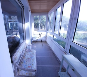 Enjoy the serene views of the surrounding landscape from this sunroom with a bench and tripod stand.