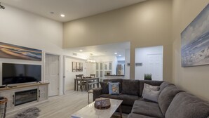 A modern living room with a grey sofa, a flat-screen TV, and a dining area with a chandelier. - Avalon. Fully renovated 2024. Pool view (Clearwater)