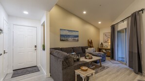 A modern living room with a grey sofa, a small wooden table, and a painting of a beach scene on the wall. - Avalon. Fully renovated 2024. Pool view (Clearwater)