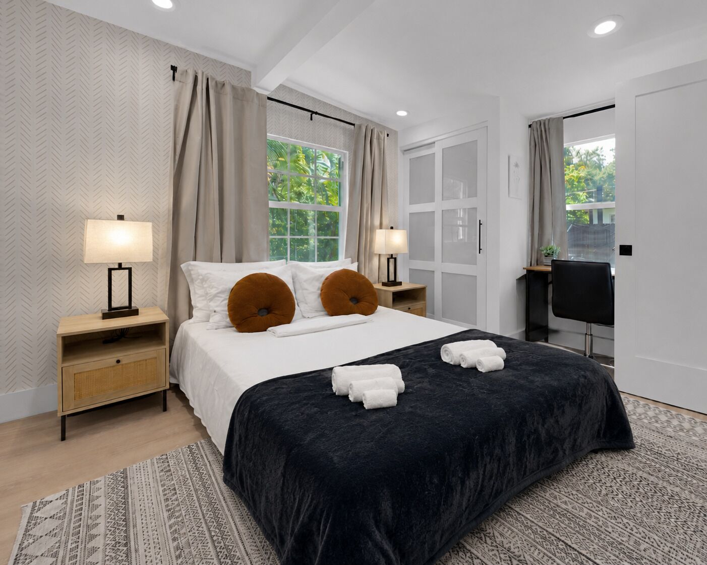Une chambre d’hôtel moderne, dotée d’un grand lit, de deux lampes de chevet, d’un bureau et offrant une vue sur la verdure environnante.