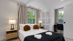 Une chambre d’hôtel moderne, dotée d’un grand lit, de deux lampes de chevet, d’un bureau et offrant une vue sur la verdure environnante.