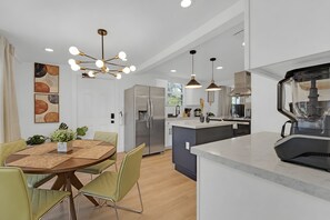 A modern kitchen with a built-in island, stainless steel appliances, pendant lighting, and a dining area with a round table and chairs.