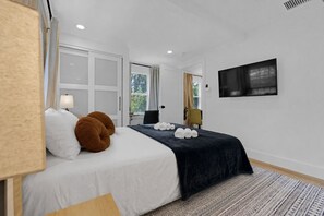 A hotel room with a bed, a TV, a window, and a door.