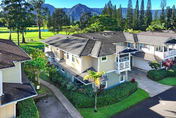 A residential building with multiple units, a well-maintained lawn, and a view of a golf course and mountains in the background.
