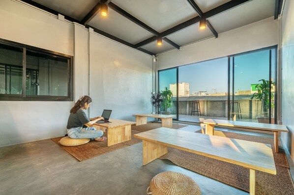 A modern interior with a large window, wooden tables, and a person using a laptop. - Ti Thong Hostel (Bangkok)