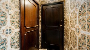 Un pasillo con dos puertas de madera, una con manija de latón y la otra con pomo redondo. Las paredes están decoradas con baldosas estampadas.