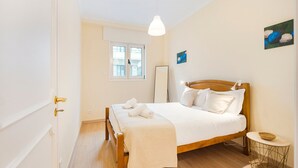 Un dormitorio con una cama de madera, ropa de cama blanca, una mesita de noche y una lámpara colgante.