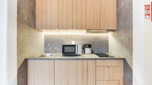 Cocina compacta con armarios de madera, un lavamanos de acero inoxidable, microondas y cafetera.