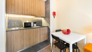 Una cocina compacta con armarios de madera, microondas y lavamanos. Hay una mesa de comedor con sillas y un tazón rojo.