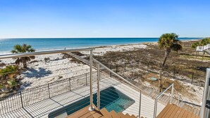 Eine Terrasse mit Pool mit Blick auf einen Strand, Palmen und einen wolkenlosen, blauen Himmel.