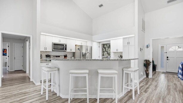A modern kitchen with white cabinetry, a central island with stools, and a microwave. - Peacock Paradise in Ocala (Ocala)