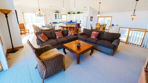 A spacious living room with a sectional sofa, a coffee table, and a wicker chair. A kitchen is visible in the background with a dining area. - WH868- Beautiful 5 bedroom, 4.5 bath vacation rental house in Corolla! (Corolla)