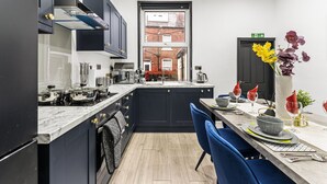 A modern kitchen with dark cabinetry, a marble countertop, and a dining area with blue chairs.