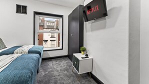 A modern bedroom with two beds, a TV mounted on the wall, and a small side table with a plant.