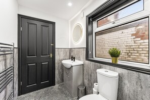 A bathroom with a black door, a white sink, a toilet, and a window with a view of a brick wall. - Stylish Designer 4 bed with Free Parking (Leeds)