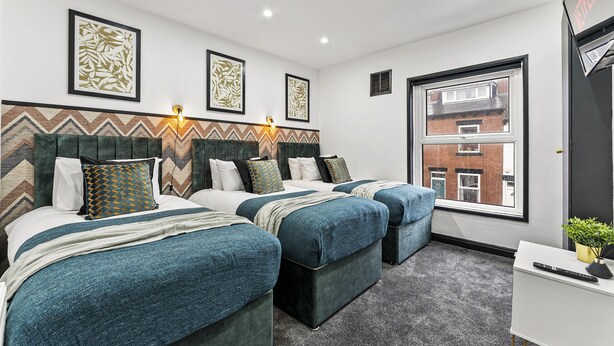 A hotel room with two beds, a desk, and a window with a view of buildings.
