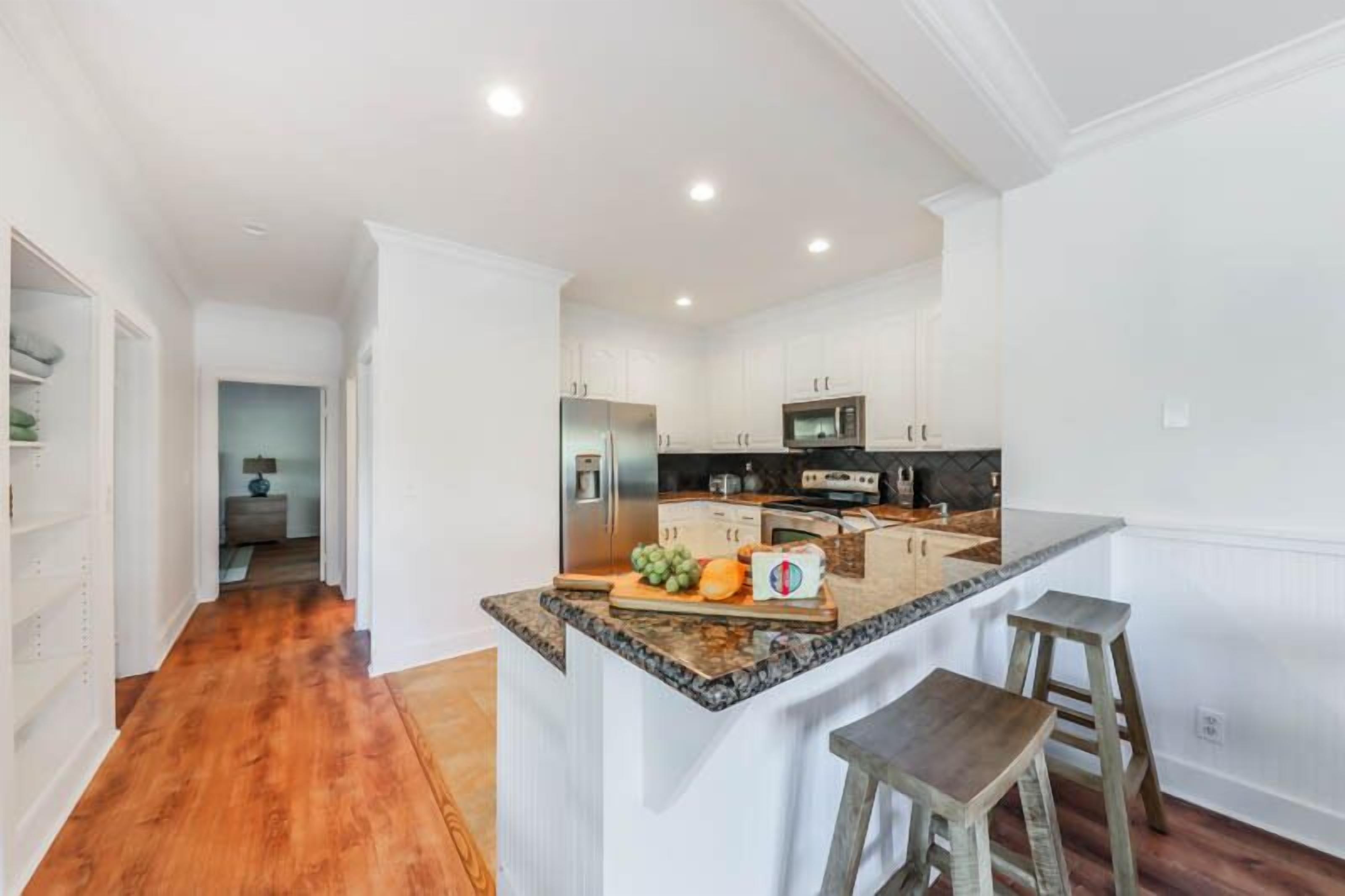 A modern kitchen with white cabinetry, a granite countertop, and a central island with stools.