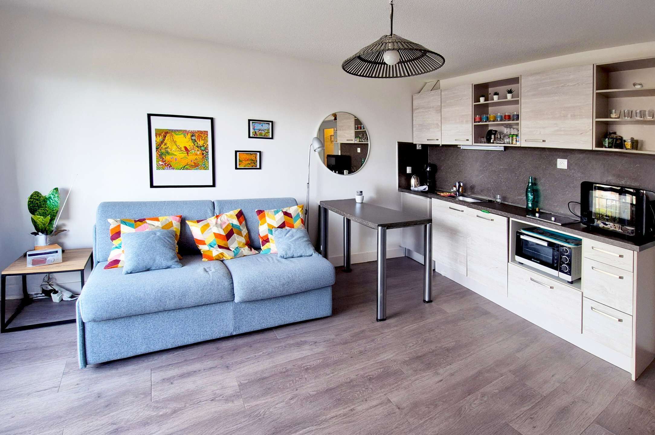 Una sala de estar moderna con sofá, mesa de comedor, zona de cocina y lámpara colgante.