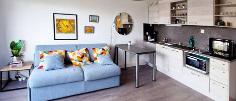 Una sala de estar moderna con sofá, mesa de comedor, zona de cocina y lámpara colgante.
