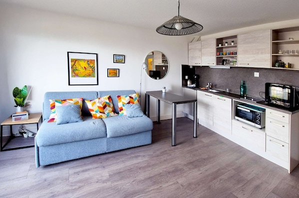 Una sala de estar moderna con sofá, mesa de comedor, zona de cocina y lámpara colgante.