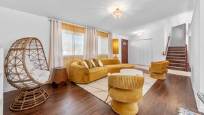 A living room with a yellow sofa, a wicker chair, and a round ottoman.