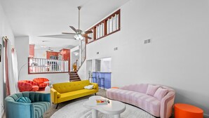 A modern living room with a yellow sofa, a pink sofa, and a teal armchair. There is a white coffee table in the center.