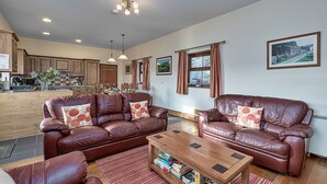 A spacious living area with leather sofas, a wooden coffee table, and a kitchen in the background. - Eithinog (Talybont)
