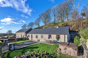 A stone building with a sloped roof, a patio with outdoor furniture, and a hot tub.
