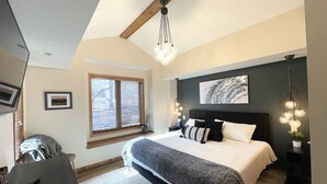 A bedroom with a large bed, a wooden headboard, a window with blinds, a bedside table, and a hanging light fixture. - Secret Room-Hot Tub-Billards-Firepit-Games-Pool access (Gal)