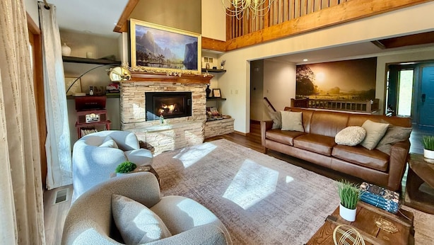 A spacious living room with a stone fireplace, a large sofa, a coffee table, and a chandelier. - Secret Room-Hot Tub-Billards-Firepit-Games-Pool access (Gal)