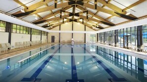 A large indoor swimming pool with a high ceiling and wooden beams, surrounded by windows and lounge chairs. - Secret Room-Hot Tub-Billards-Firepit-Games-Pool access (Gal)