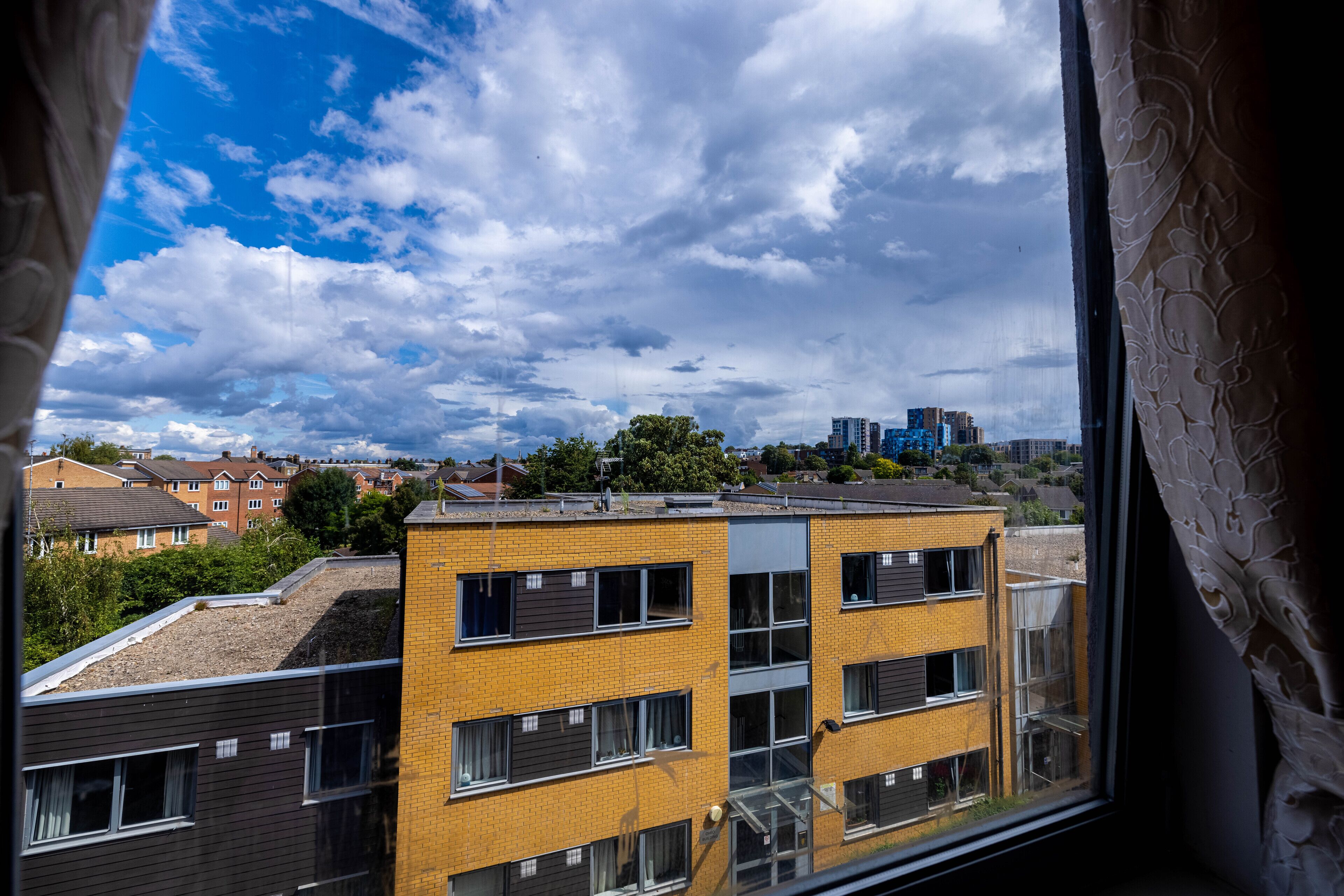 A view of a multi-story building with a brick facade and multiple windows, viewed from a window with a curtain.