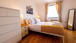 A bedroom with a bed, bedside lamps, a dresser, a window with curtains, and a wall-mounted picture.