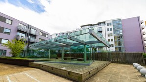 A modern outdoor patio area with a glass enclosure, wooden deck, and a view of surrounding buildings.