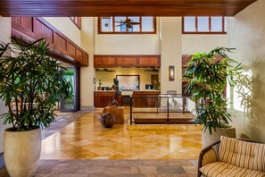 A spacious lobby with a reception desk, large potted plants, a staircase, and a ceiling fan.