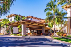 A hotel with a covered entrance, palm trees, and a well-maintained lawn.