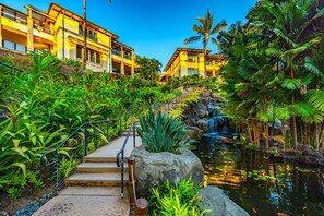 Ein Resort mit Wasserfall, üppiger Vegetation und einem mehrstöckigen Gebäude mit Balkonen.