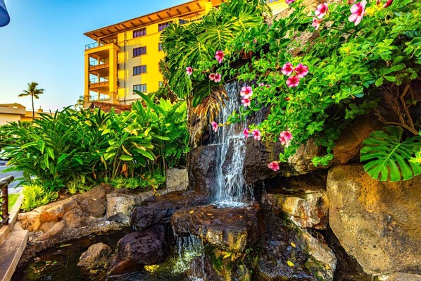 A waterfall cascading over rocks with lush greenery and pink flowers.