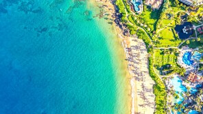 An aerial view of a coastal resort with a beach, swimming pools, and lush landscaping.