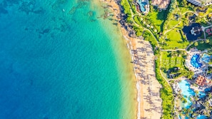An aerial view of a resort with a beach, clear turquoise water, and a pool area.