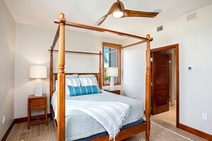 A four-poster bed with a wooden frame, a nightstand with a lamp, and a door leading to another room.