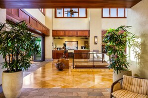 Eine geräumige Lobby mit einer Rezeption, großen Kübelpflanzen und einer hohen Decke mit Holzbalken.