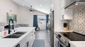 Une cuisine moderne dotée d’un îlot central, d’un réfrigérateur et d’une cuisinière. On y trouve également un coin repas avec un canapé et une vue sur l’extérieur.