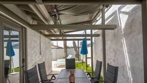 Une terrasse couverte avec une table et des chaises, une pergola au-dessus et une vue sur le jardin arrière.