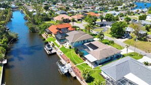 An aerial view of a residential area with houses, a river, and a dock with boats. - VRCC Villa Paradise Palms (Cape Coral)
