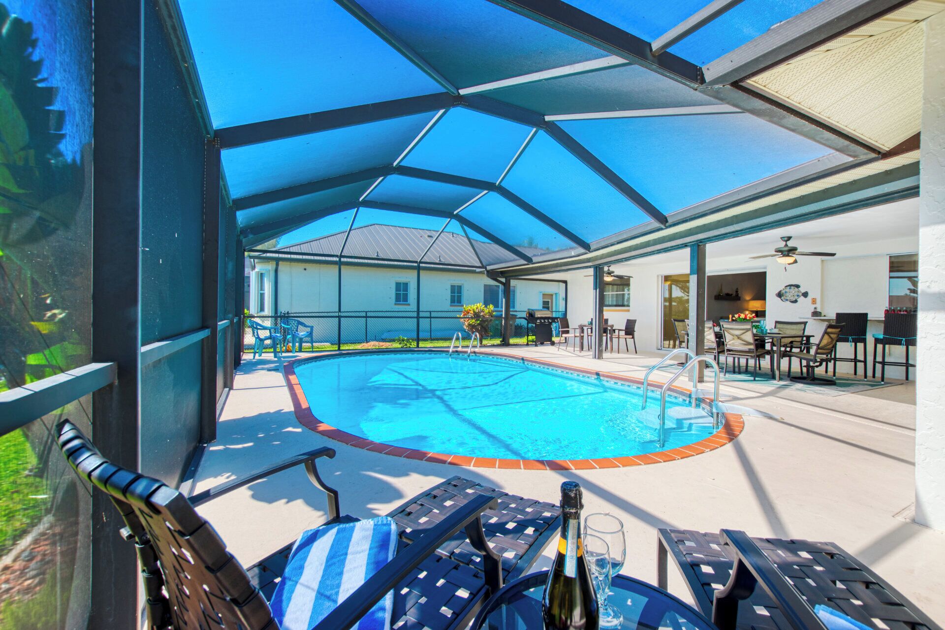 A covered outdoor swimming pool area with lounge chairs, a bar, and a grill.