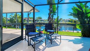A balcony with two chairs and a small table, overlooking a swimming pool and a residential area. - VRCC Villa Paradise Palms (Cape Coral)