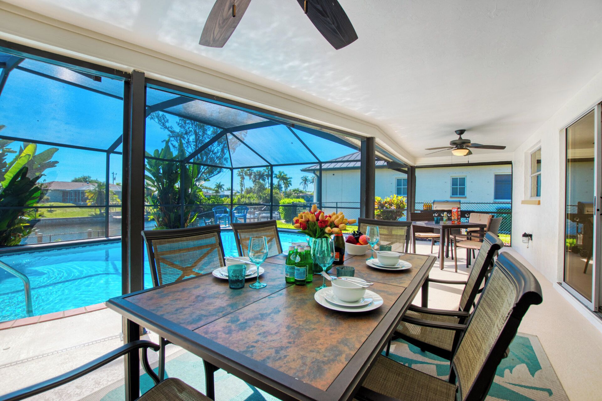 A dining area with a view of a swimming pool, large windows, and a ceiling fan.